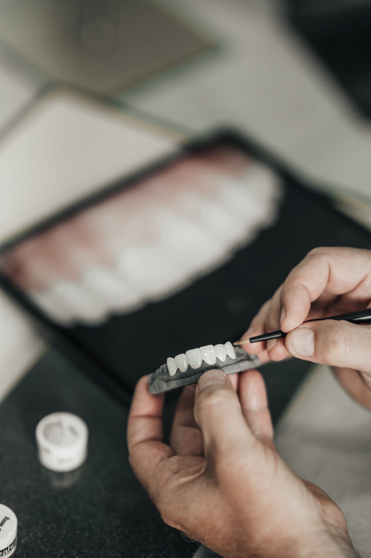 An ACE DNTL ceramist hand-painting a veneer arch with the patient smile photograph on the screen behind